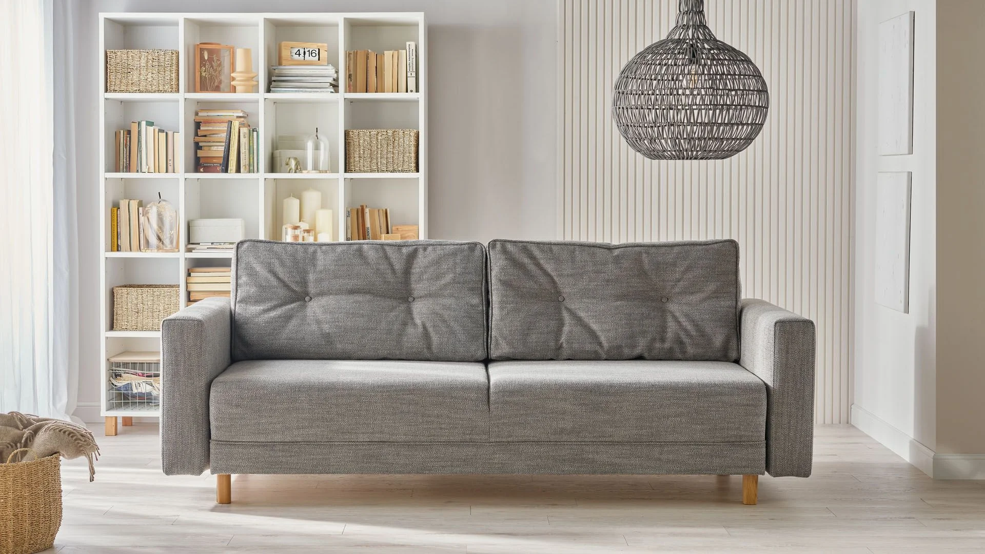 Szara sofa na tle białego regału z książkami i lamelowej ściany